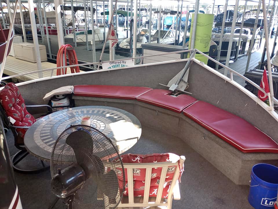 Interior seating area of a 1990 Lazy Days 60' high bow wide body houseboat featuring a round table, red cushions, and a fan.