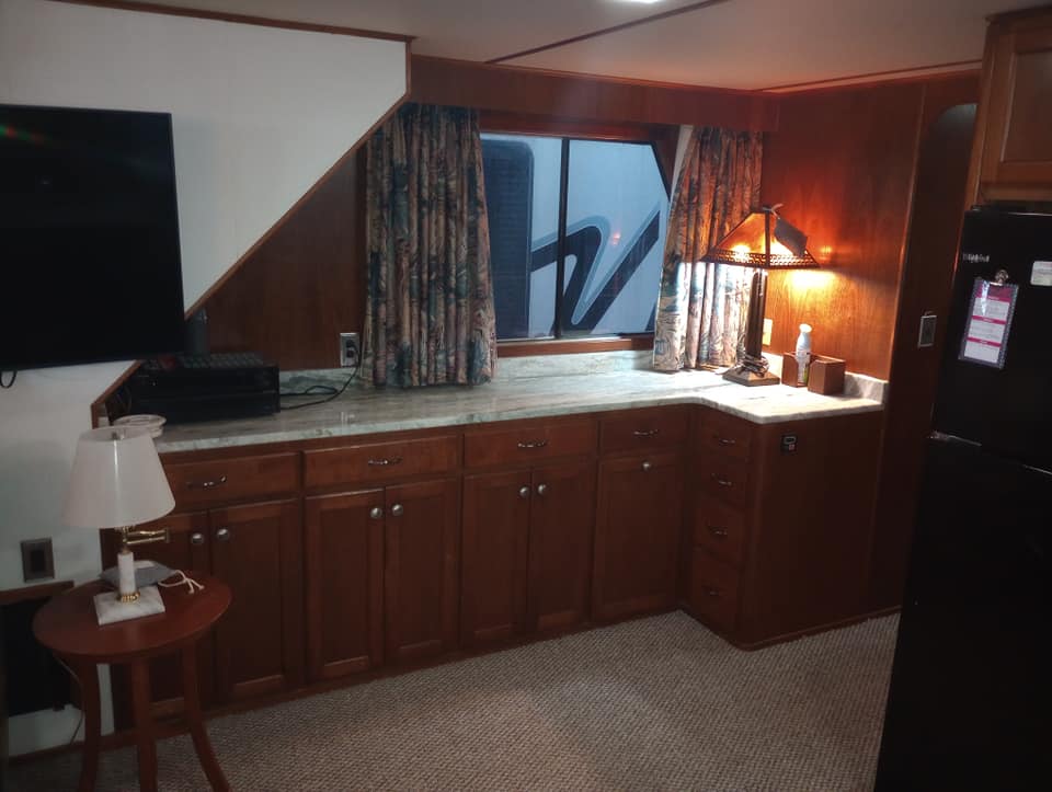 Interior view of a galley in a 1990 Lazy Days houseboat, featuring wooden cabinetry, granite countertops, a TV, and decorative curtains.