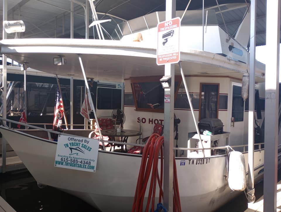 1990 Lazy Days 60' widebody houseboat docked at Cherokee Marina, featuring a 'So Hot' sign and various flags.