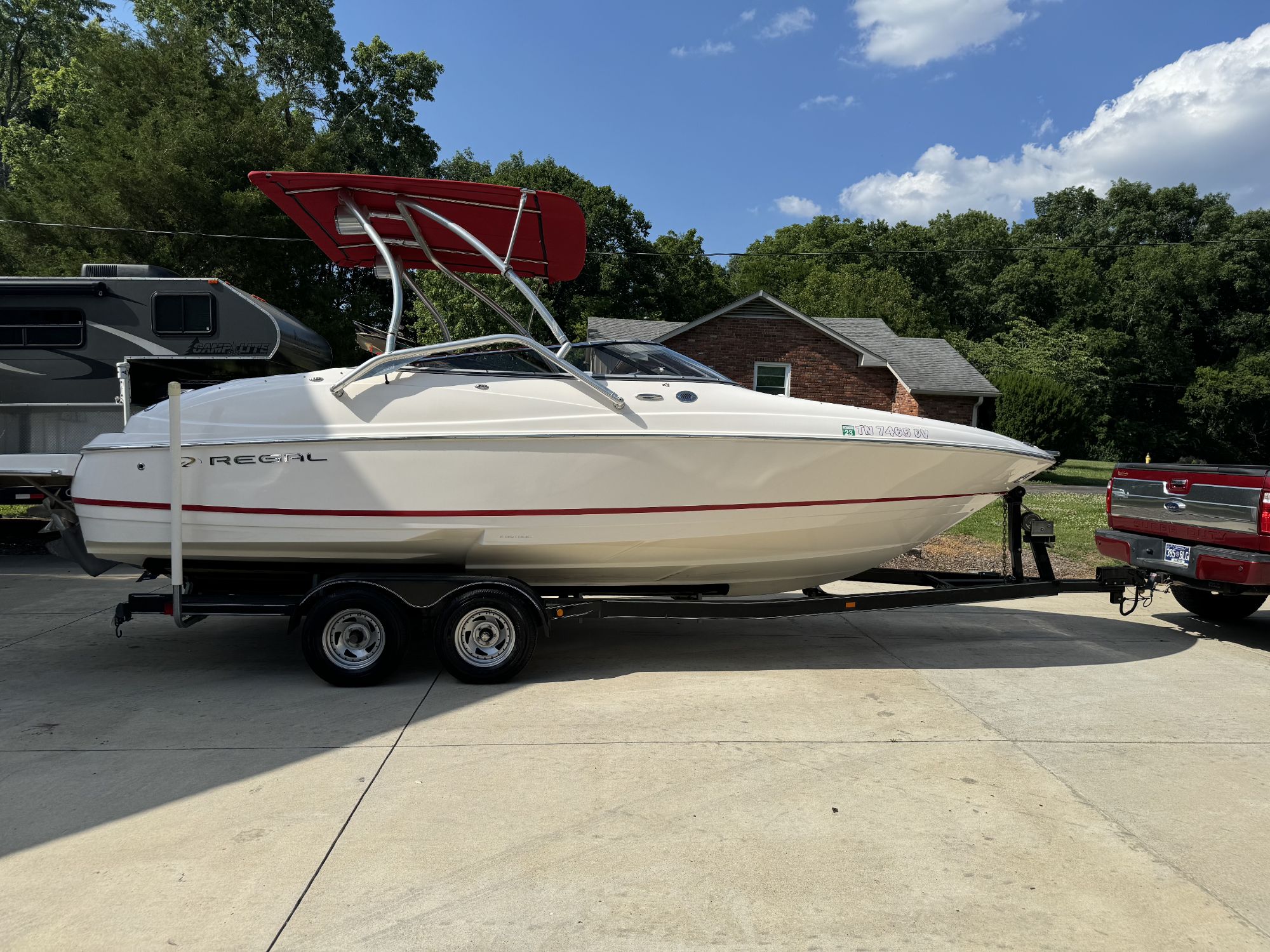 A white Regal boat with a red canopy on a trailer, parked on a driveway with a house and trees in the background.