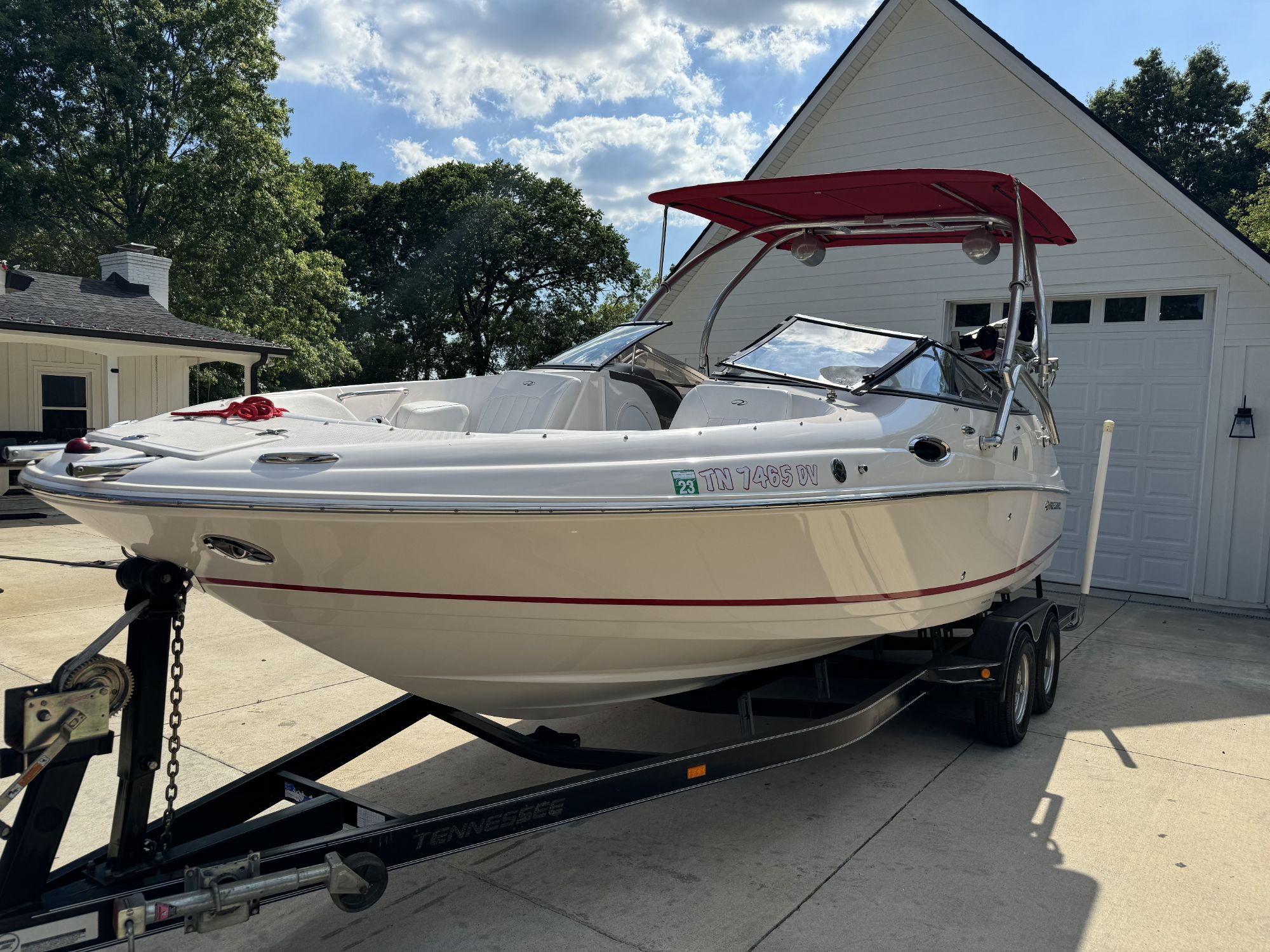 A 2007 Regal 2400 Bowrider boat with a red Bimini top, parked on a tandem axle trailer in a driveway, showcasing its sleek design and features.
