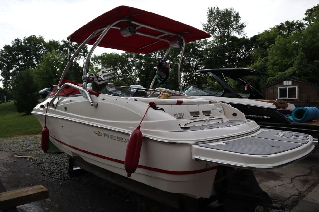 A 2007 Regal 2400 Bowrider boat parked on a gravel surface, featuring a wakeboard tower and a red Bimini top.