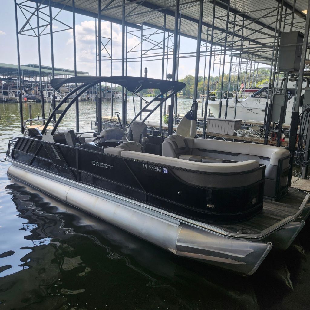 Black Crest 250 Tritoon boat docked at a marina with spacious seating and a folding tower.