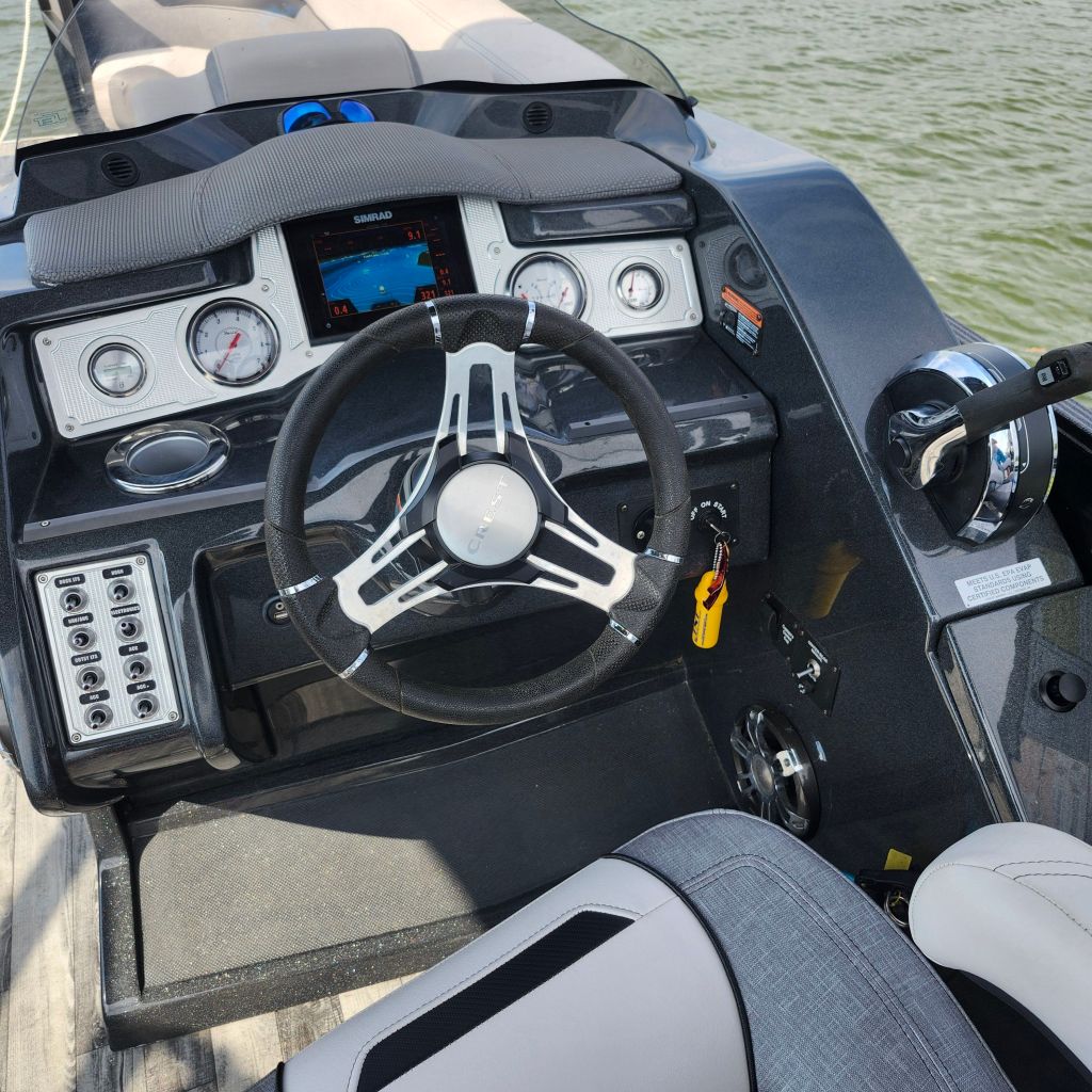 A close-up view of the helm of a 2019 Crest 250 Caliber boat featuring a steering wheel, Simrad GPS display, and various control panels, with water in the background.