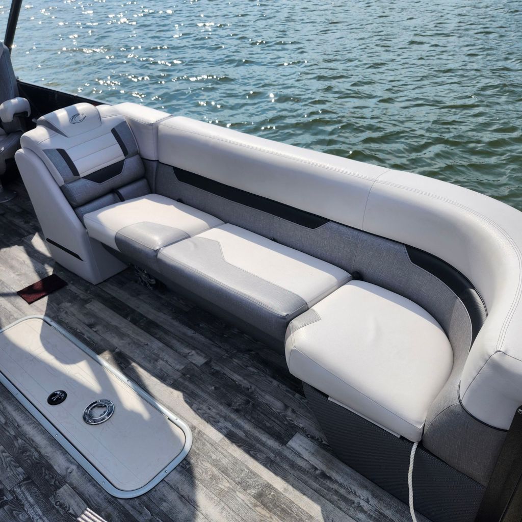 A spacious seating area on a 2019 Crest 250 Caliber Tritoon, featuring gray and white cushions, set against a backdrop of sparkling water.