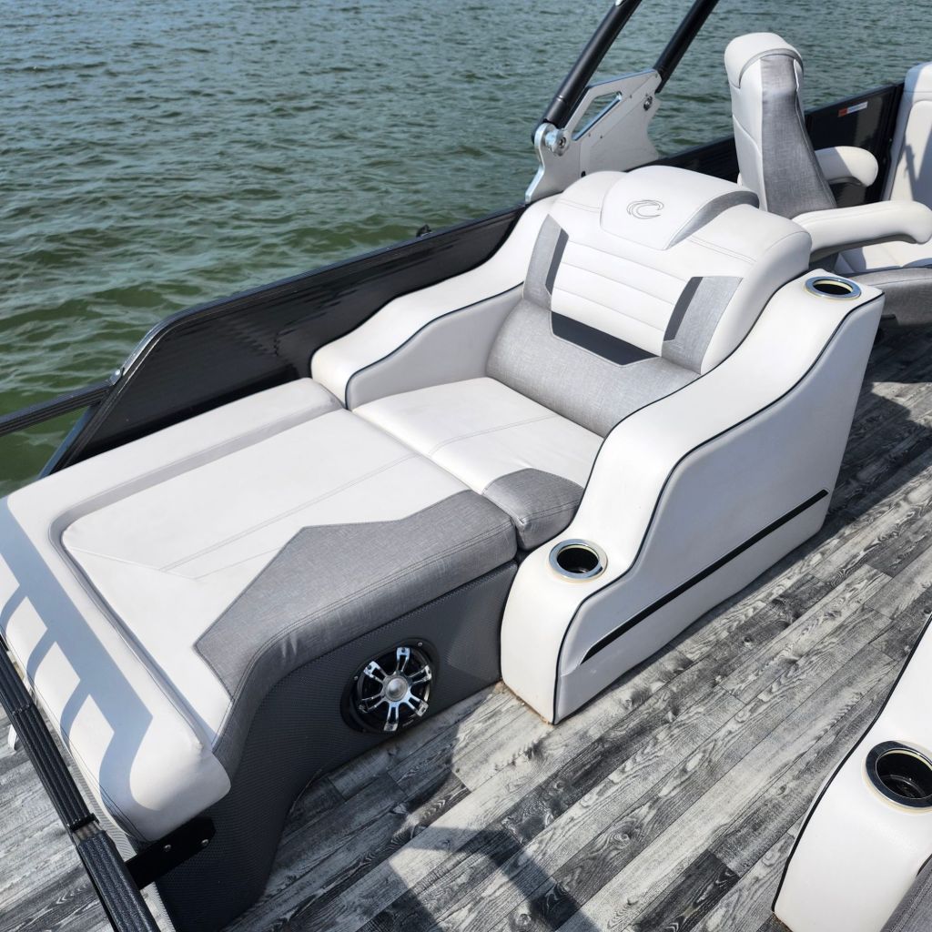 Spacious seating area on a 2019 Crest Caliber 250 Tritoon boat, featuring gray and white upholstery and a built-in cup holder, with a view of the water in the background.