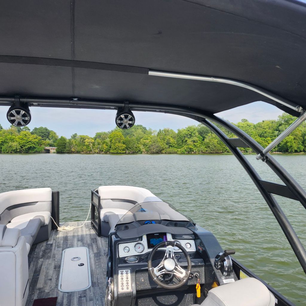 Interior view of a 2019 Crest 250 Caliber tritoon boat, showcasing spacious seating and control console, with water and trees in the background.