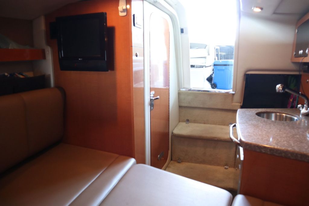 Interior view of a 2009 Chaparral 250 Signature boat, featuring a galley area with a sink, TV mounted on the wall, and a small staircase leading to the exterior.