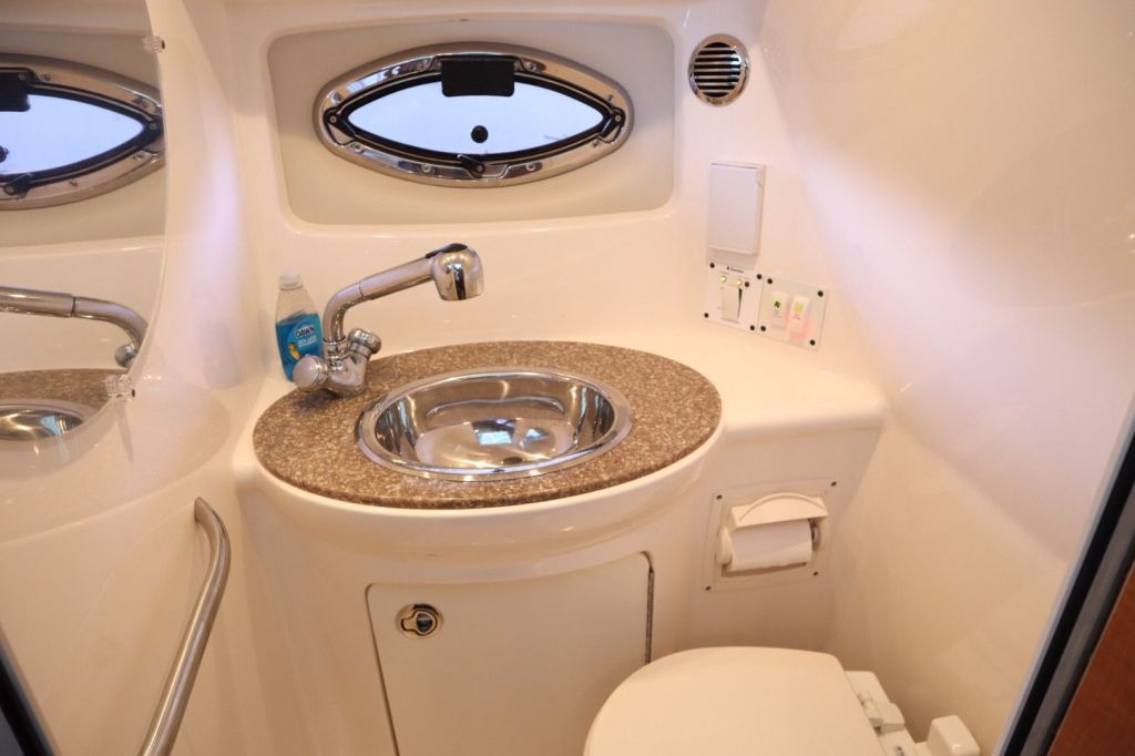 Interior view of a boat's wet head featuring a sink, toilet, and cabinetry.