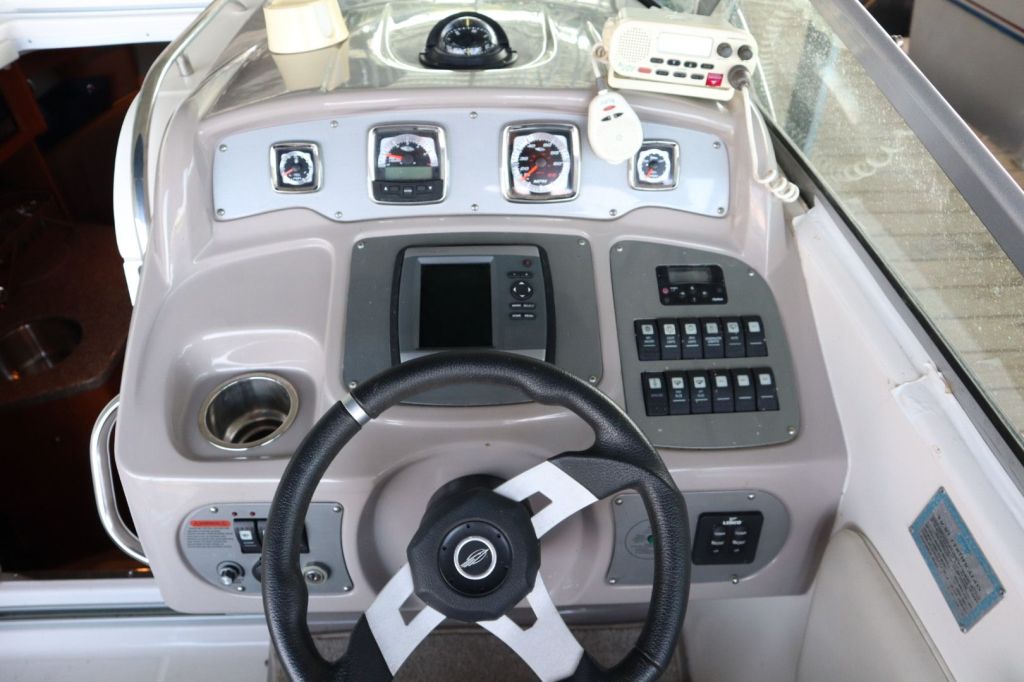 Interior view of a boat's helm featuring a steering wheel, gauges, control panel, and a cup holder.