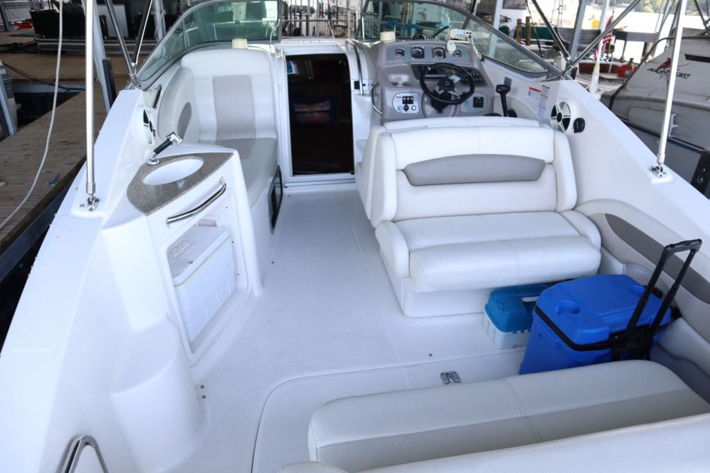 Interior view of a 2009 Chaparral Signature 250 boat, showing the cockpit with white seating, a helm with controls, and a small sink area.