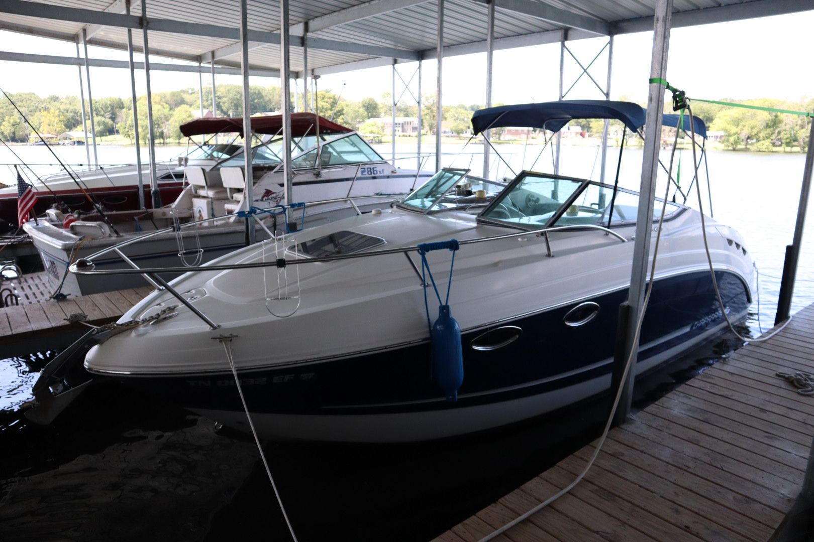 A white and dark blue boat docked at a marina, surrounded by other boats and a serene water view in the background.