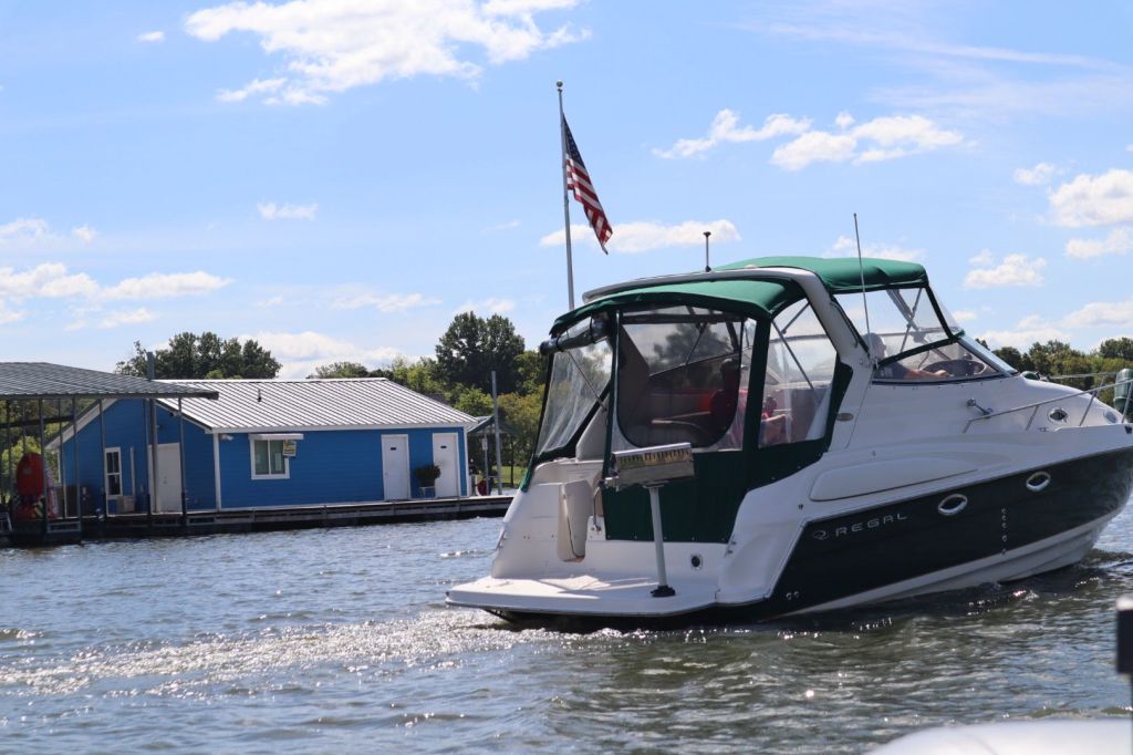 A Regal 2860 Commodore boat with a green and white exterior is shown near a blue houseboat on the water under a clear sky.