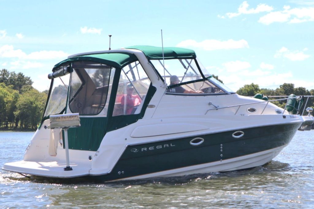 A Regal 2860 Commodore boat on the water, featuring a green canopy and a sleek white hull, with a person at the helm.