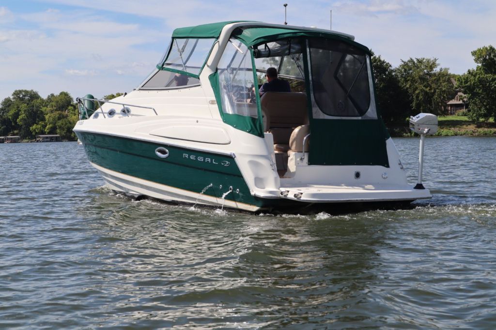 A Regal 2860 Commodore boat cruising on a lake with a green canopy and a person at the helm.