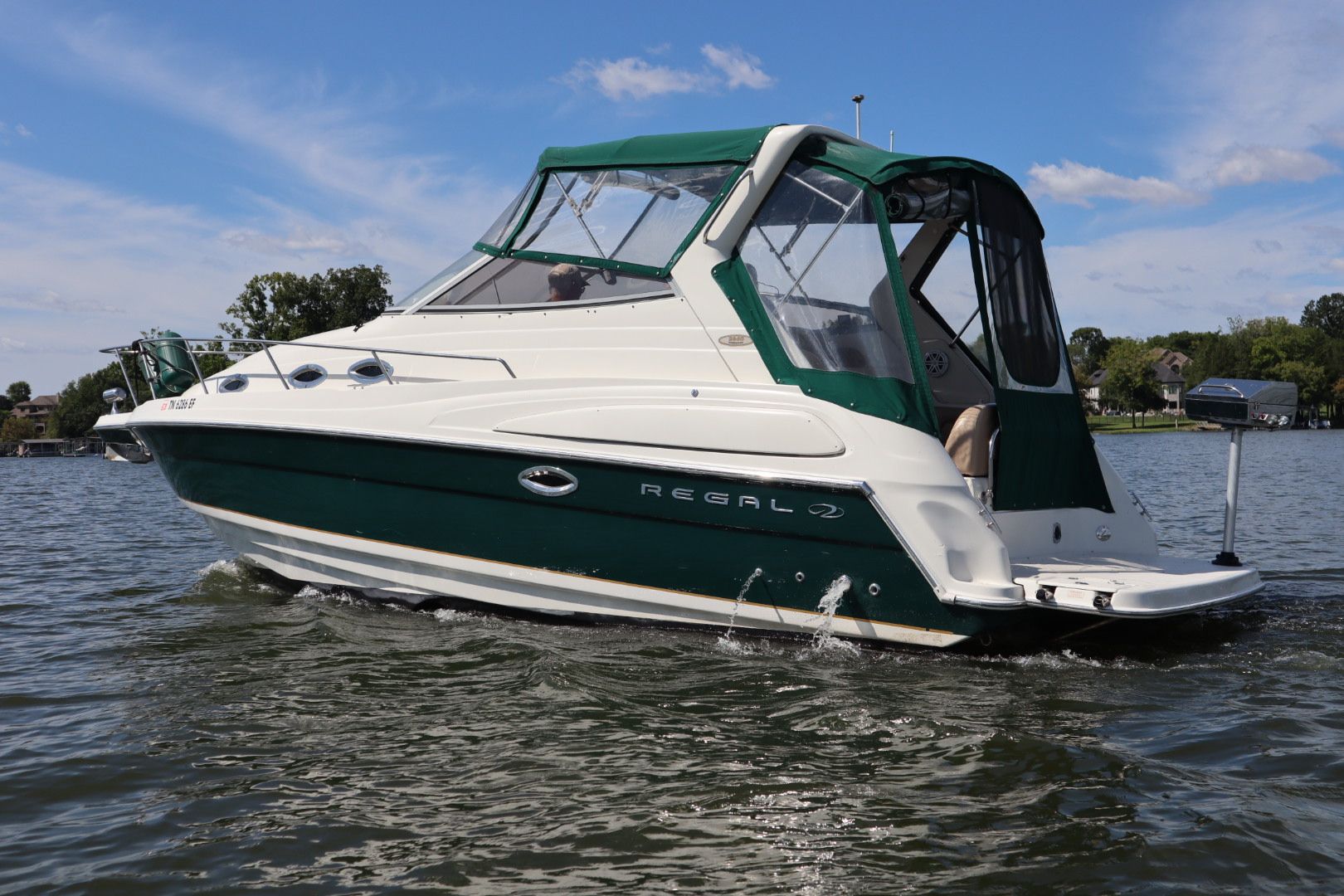 A Regal 2400 Bowrider boat with a green canopy, cruising on a lake on a clear day.
