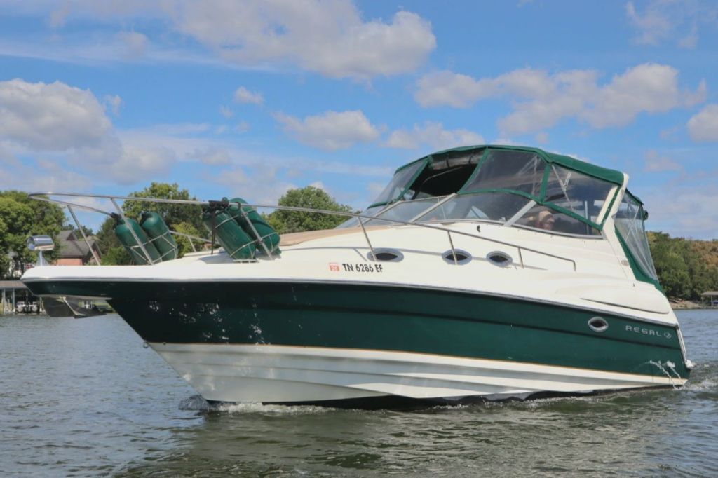 A Regal 2860 Commodore boat cruising on water with a blue sky and clouds in the background.
