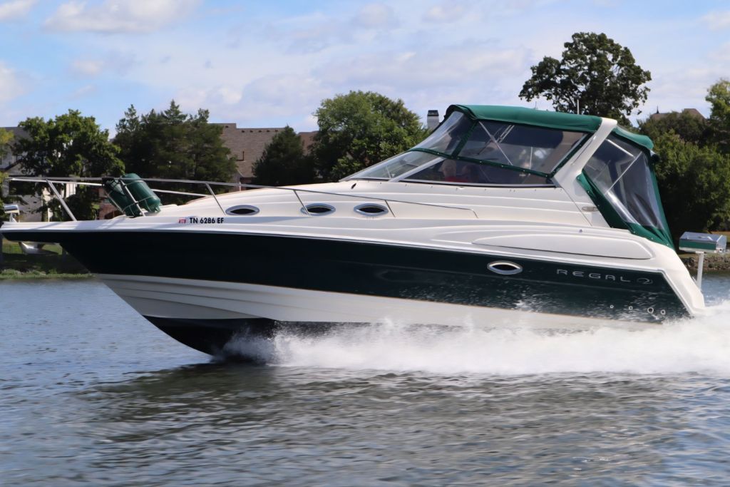 A Regal 2860 Commodore boat cruising on water with a green canopy and white hull.