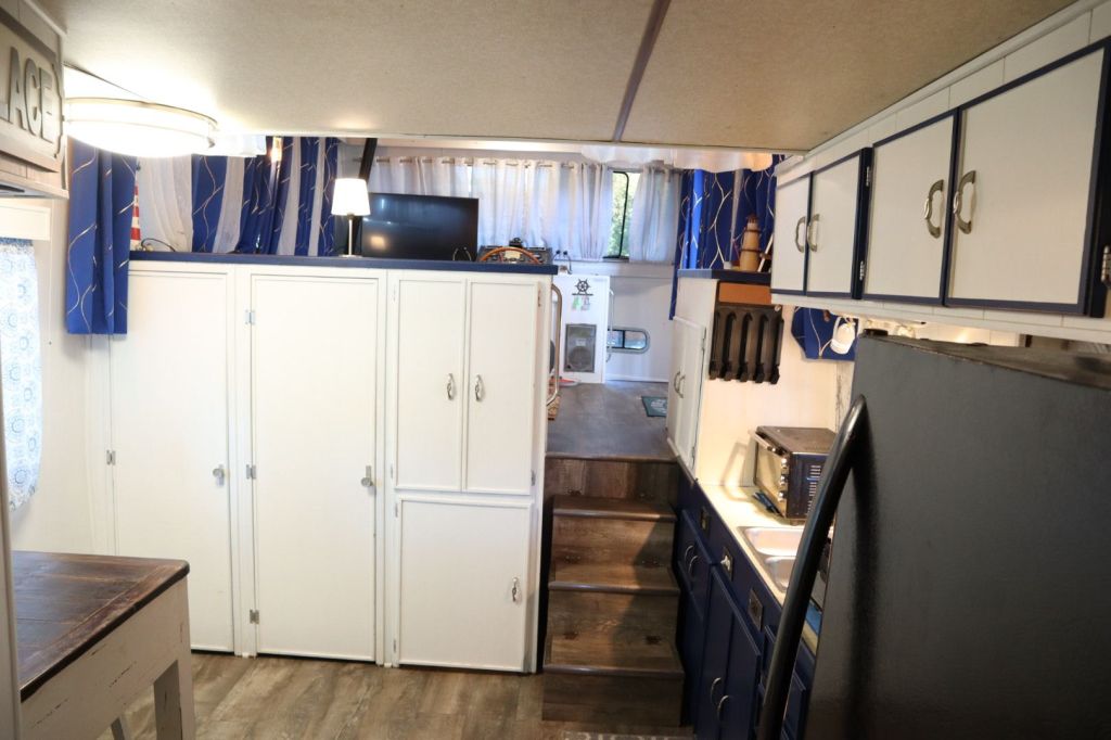 Interior view of a houseboat kitchen area featuring white cabinets, blue accents, a dining table, and various appliances.