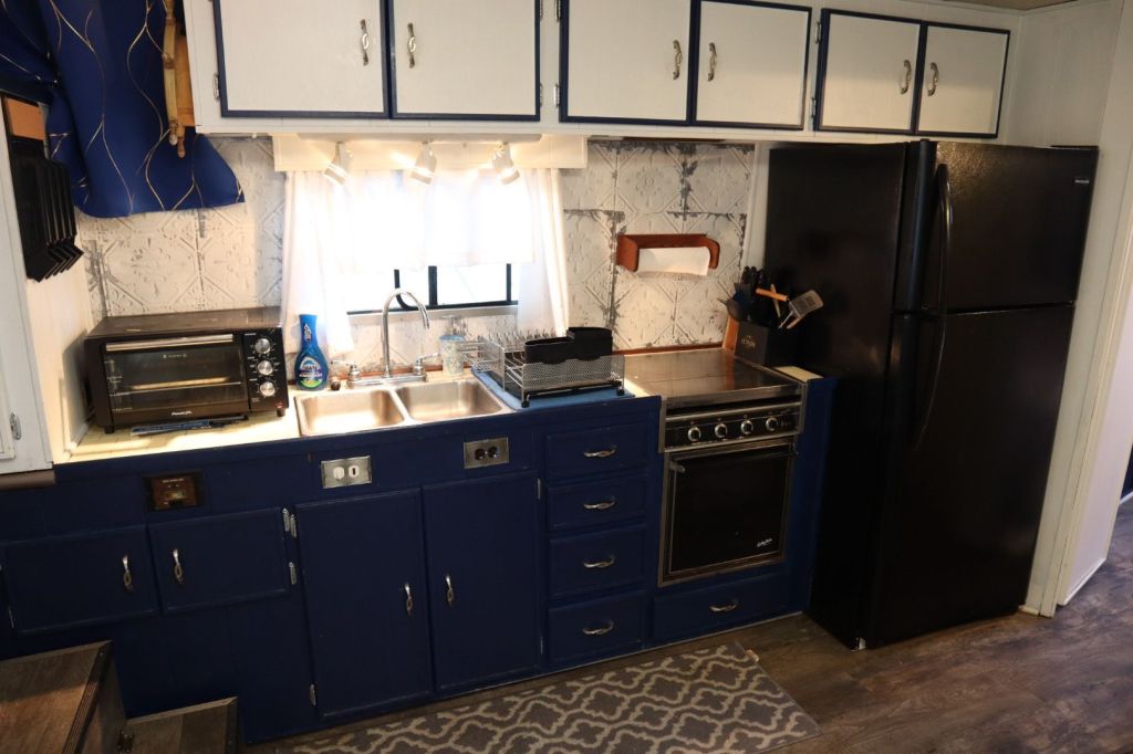 Kitchen area of a houseboat featuring a blue and white design, equipped with a sink, countertop, microwave, oven, and refrigerator.
