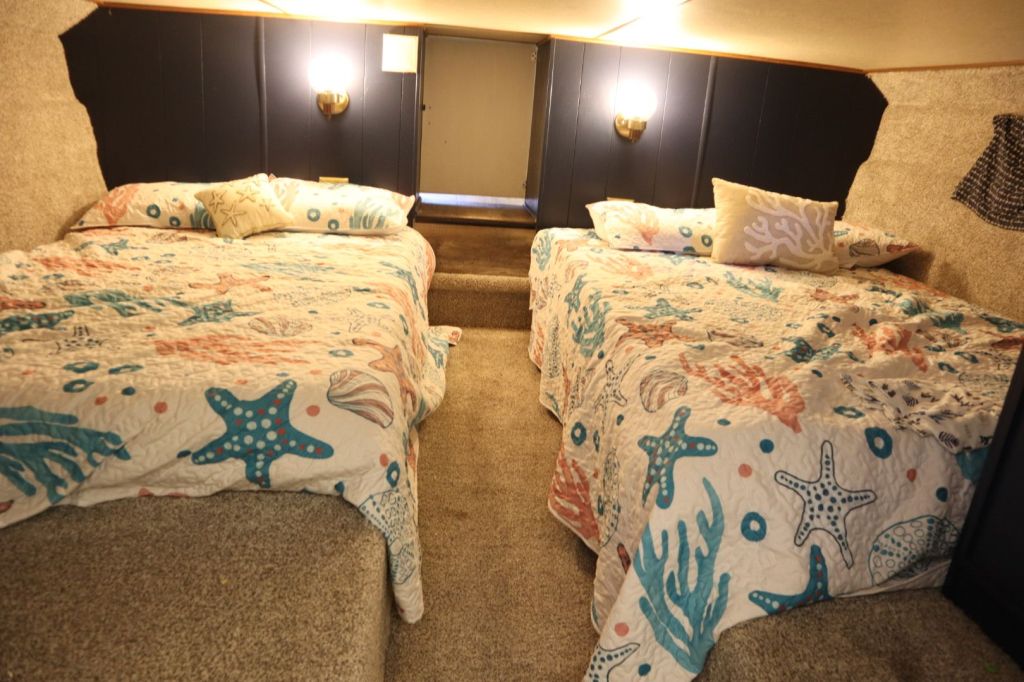 Interior view of the cuddy cabin on a houseboat, featuring two full-size beds with colorful marine-themed bedspreads.