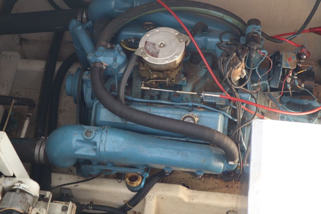 Close-up view of a blue Crusader 350ci engine installed in a boat, showing various components including hoses, wiring, and a carburetor.