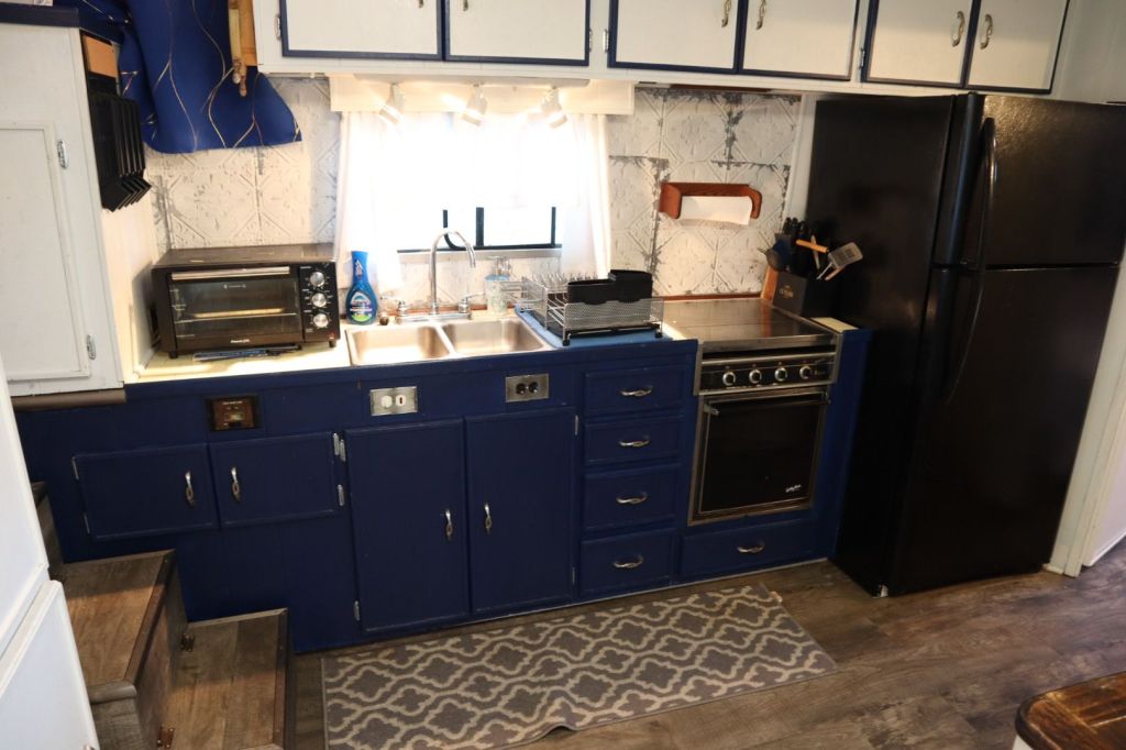 Interior view of a houseboat kitchen featuring blue cabinetry, a stainless steel sink, a black refrigerator, an oven, and a small countertop appliance.