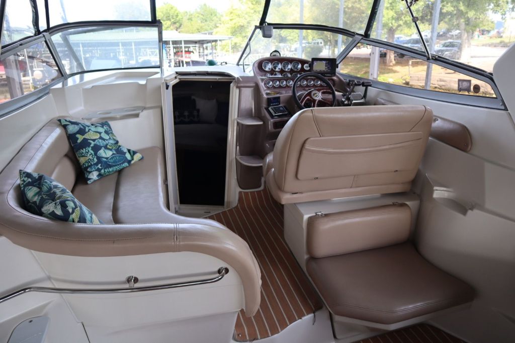 Interior view of the cockpit area of a 2002 Regal 2860 Commodore boat, featuring a leather-wrapped helm with gauges, a comfortable bench seat with decorative pillows, and a storage compartment.