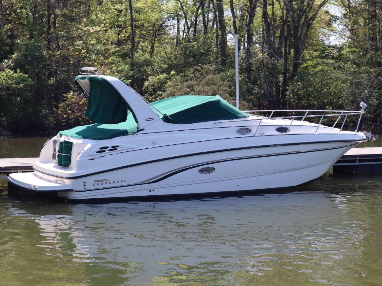 A white Chaparral boat moored at a dock, featuring a green canopy and surrounded by trees and water.